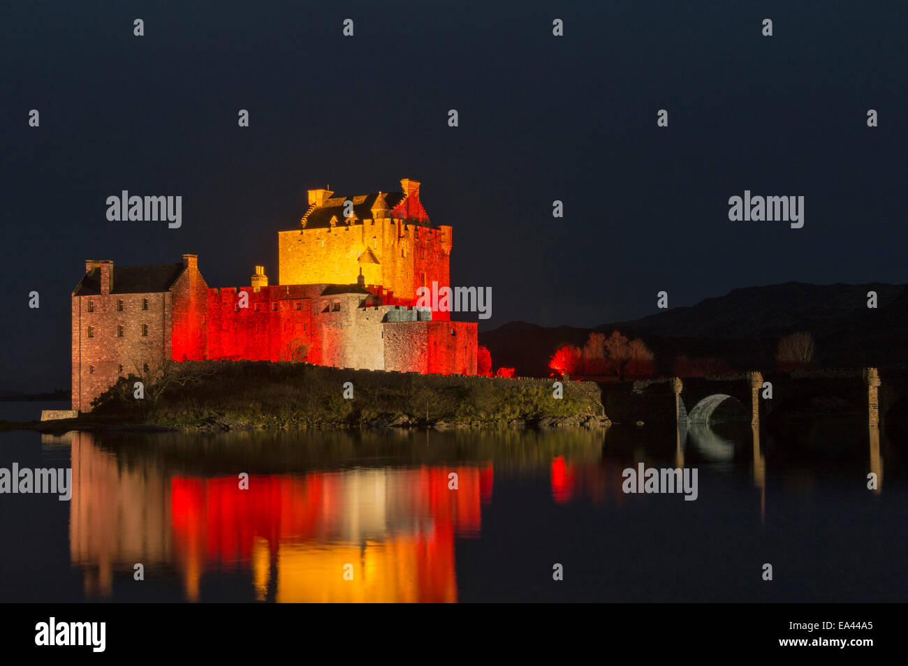 EILEAN DONAN CASTLE SCOTLAND AND BRIDGE WITH EVENING  RED LIGHTS RELECTED ON THE SEA LOCH  FOR ARMISTICE DAY NOVEMBER 11 2014 Stock Photo