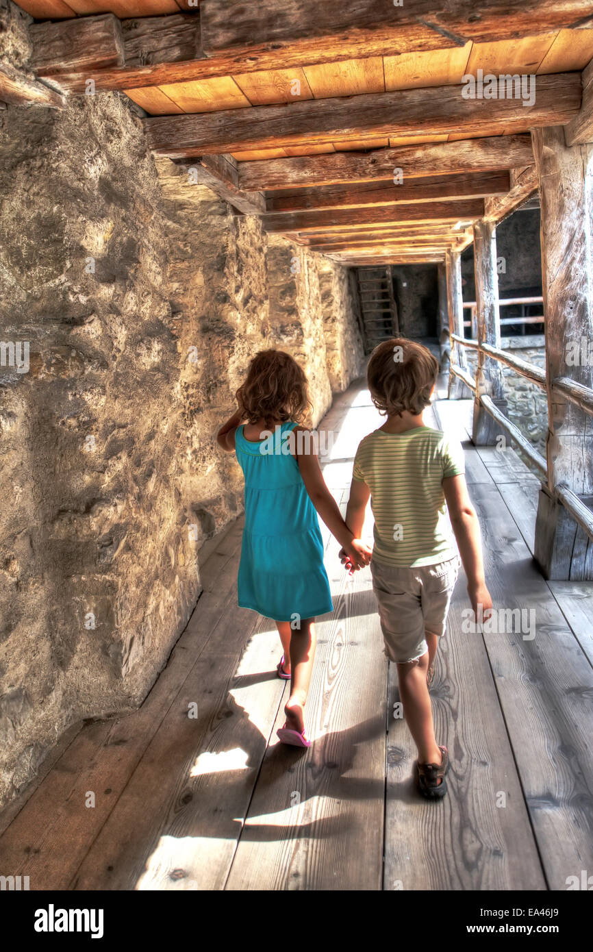 Young children hold hands while walking through an old castle. Stock Photo