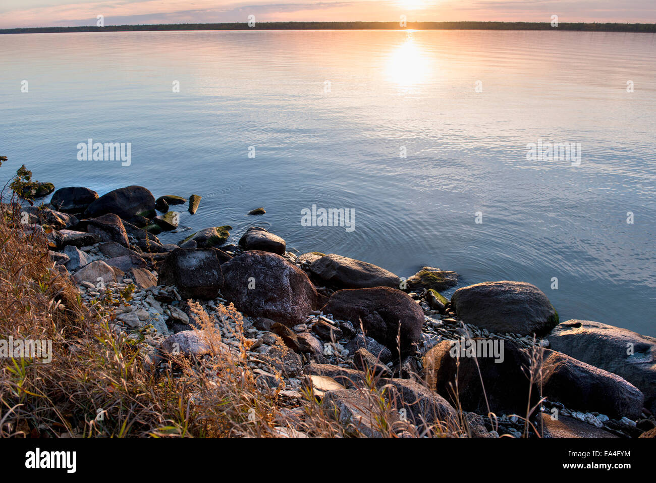 The setting sun reflects on the tranquil water with rocks along the ...