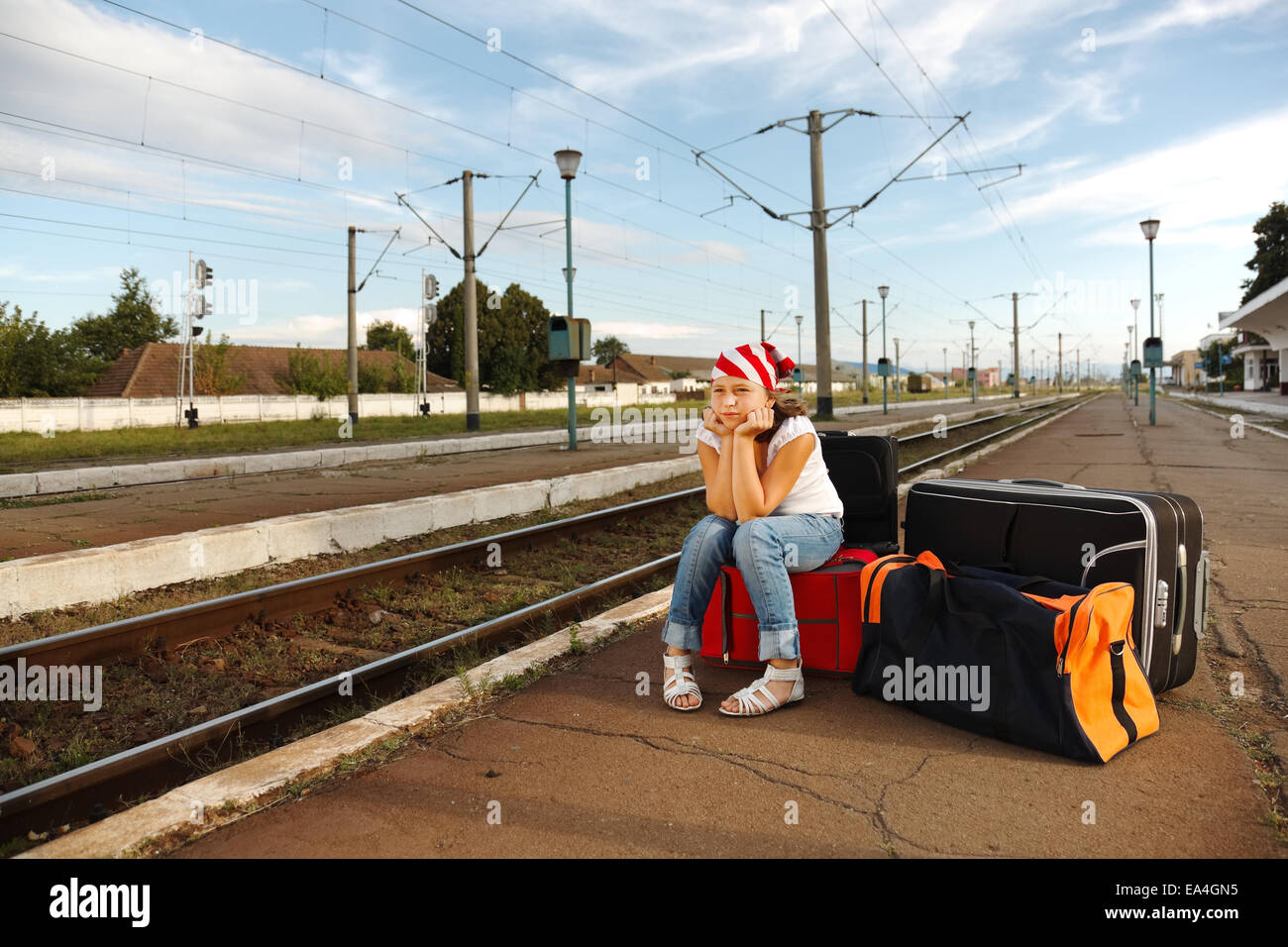 Young girl sitting on luggage and waiting for train in the station Stock Photo