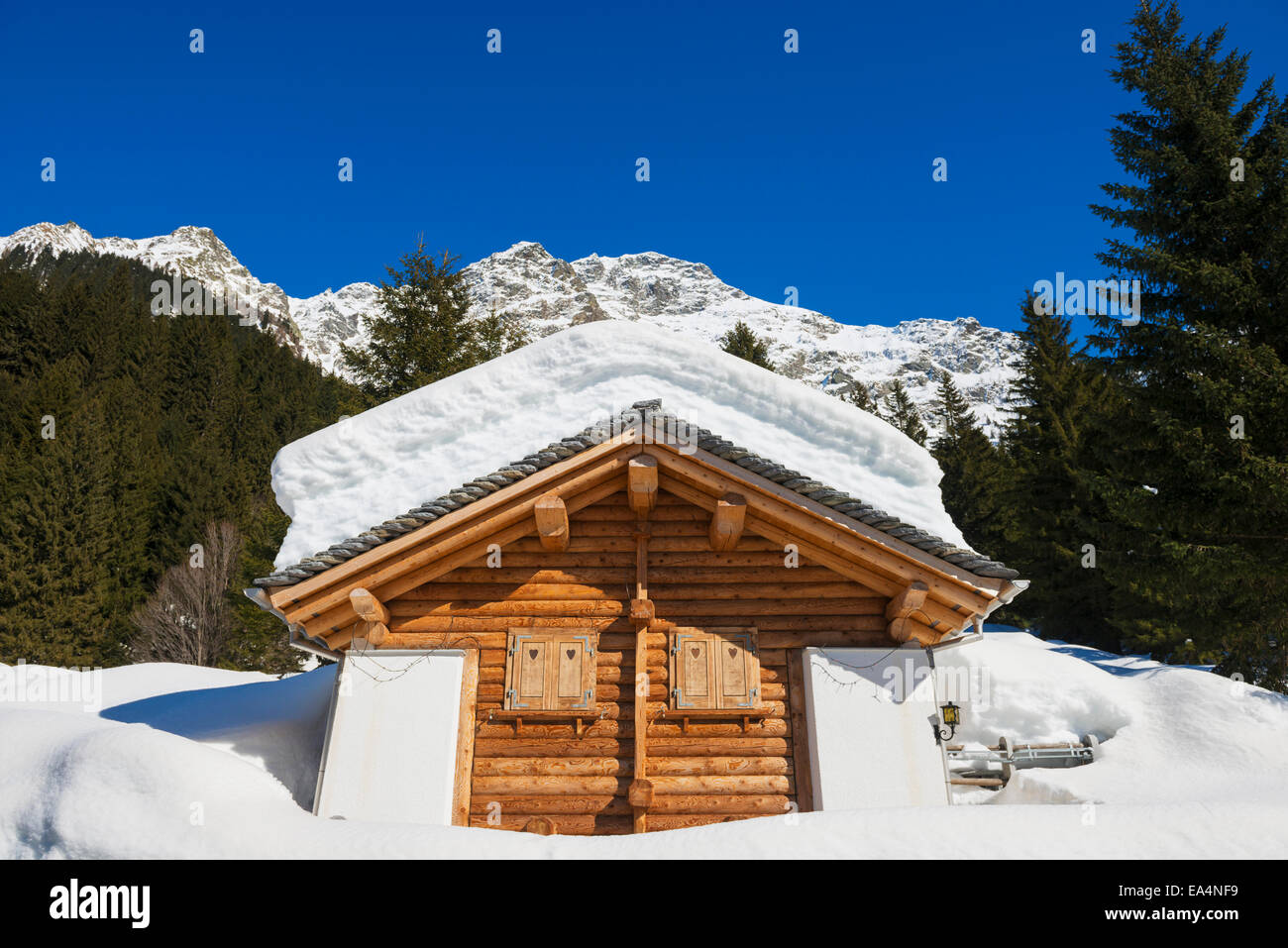 Snow covered log cabin with a mountain range in the background; San Bernardino, Grisons, Switzerland Stock Photo