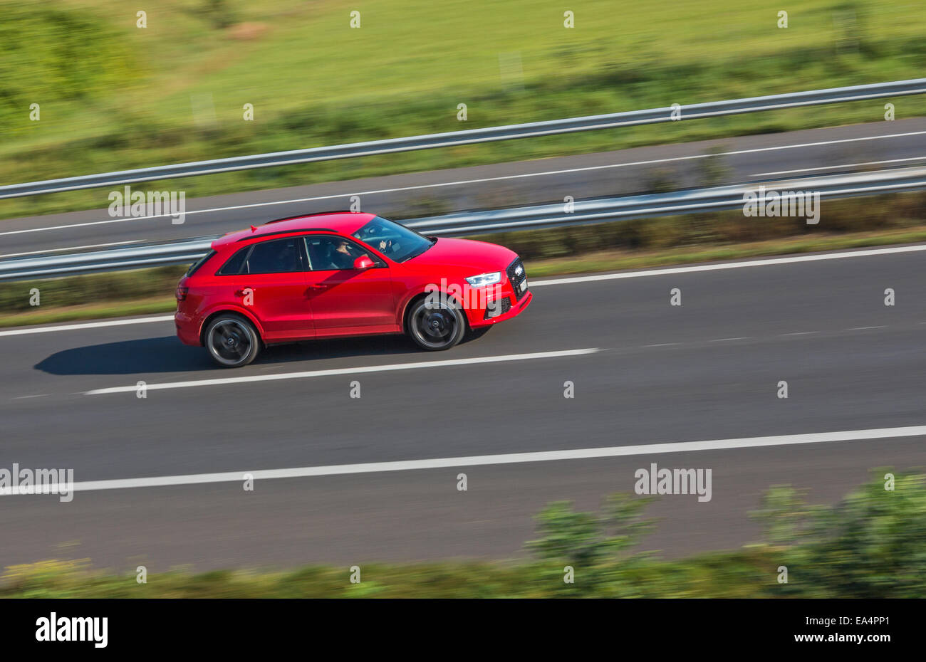 A red saloon car speeding along a motorway. Motion blur used to give a sense of speed. Stock Photo