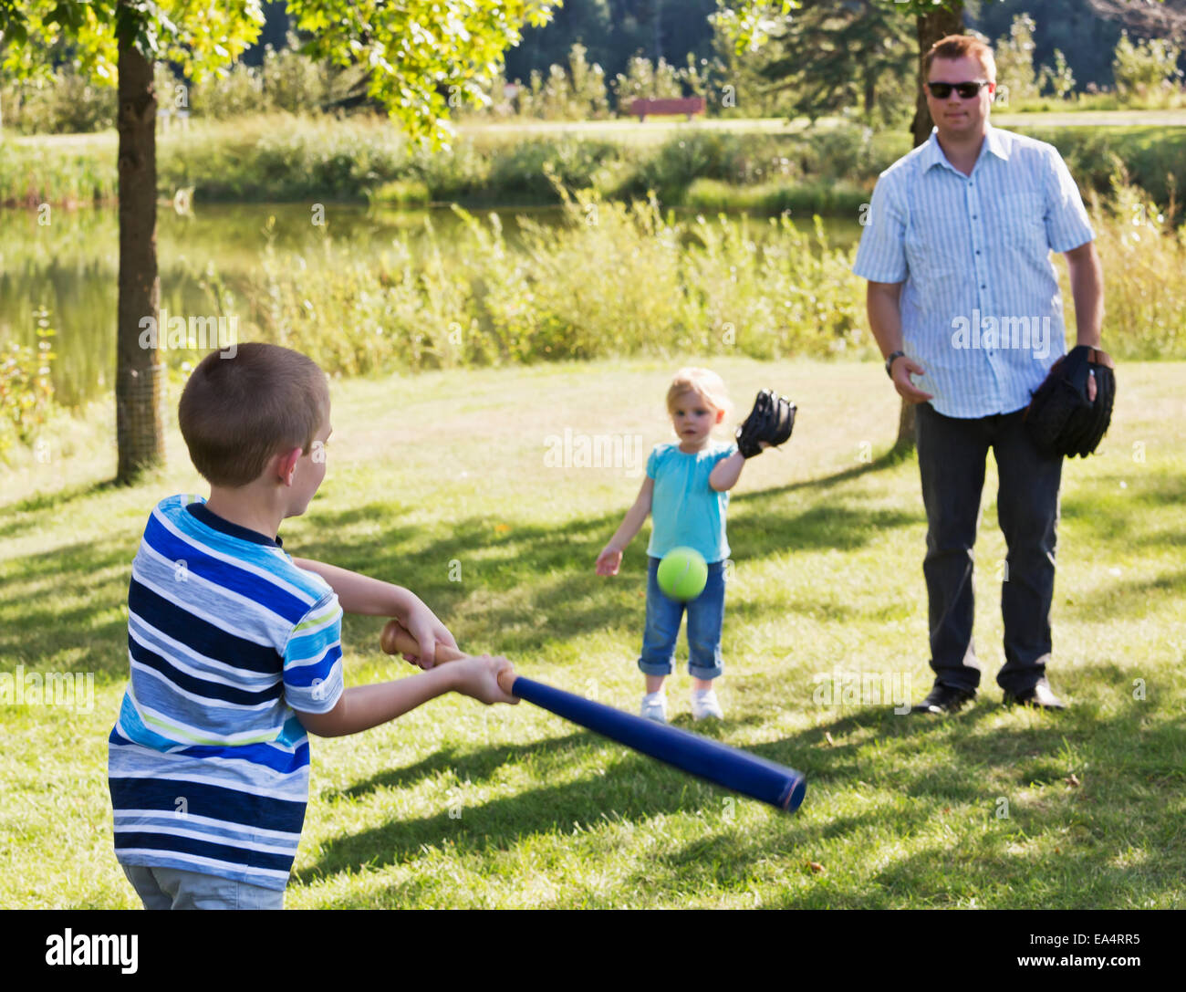 Father, son and daughter playing baseball in a park; Edmonton, Alberta, Canada Stock Photo