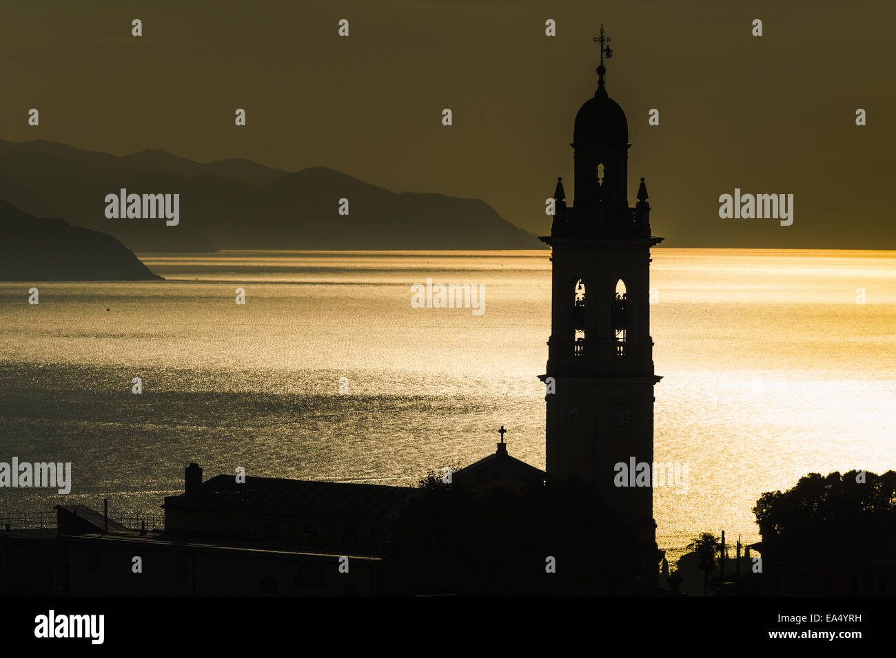 Golden sunlight reflected on water at dusk with tower of church; San Lorenzo della Costa, Liguria, Italy Stock Photo
