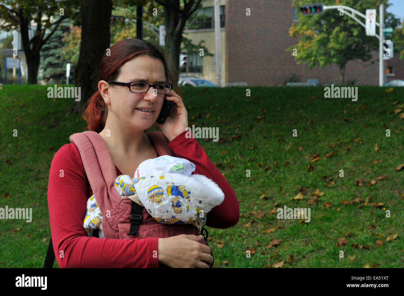 A mother carrying a baby and using a mobile phone Stock Photo