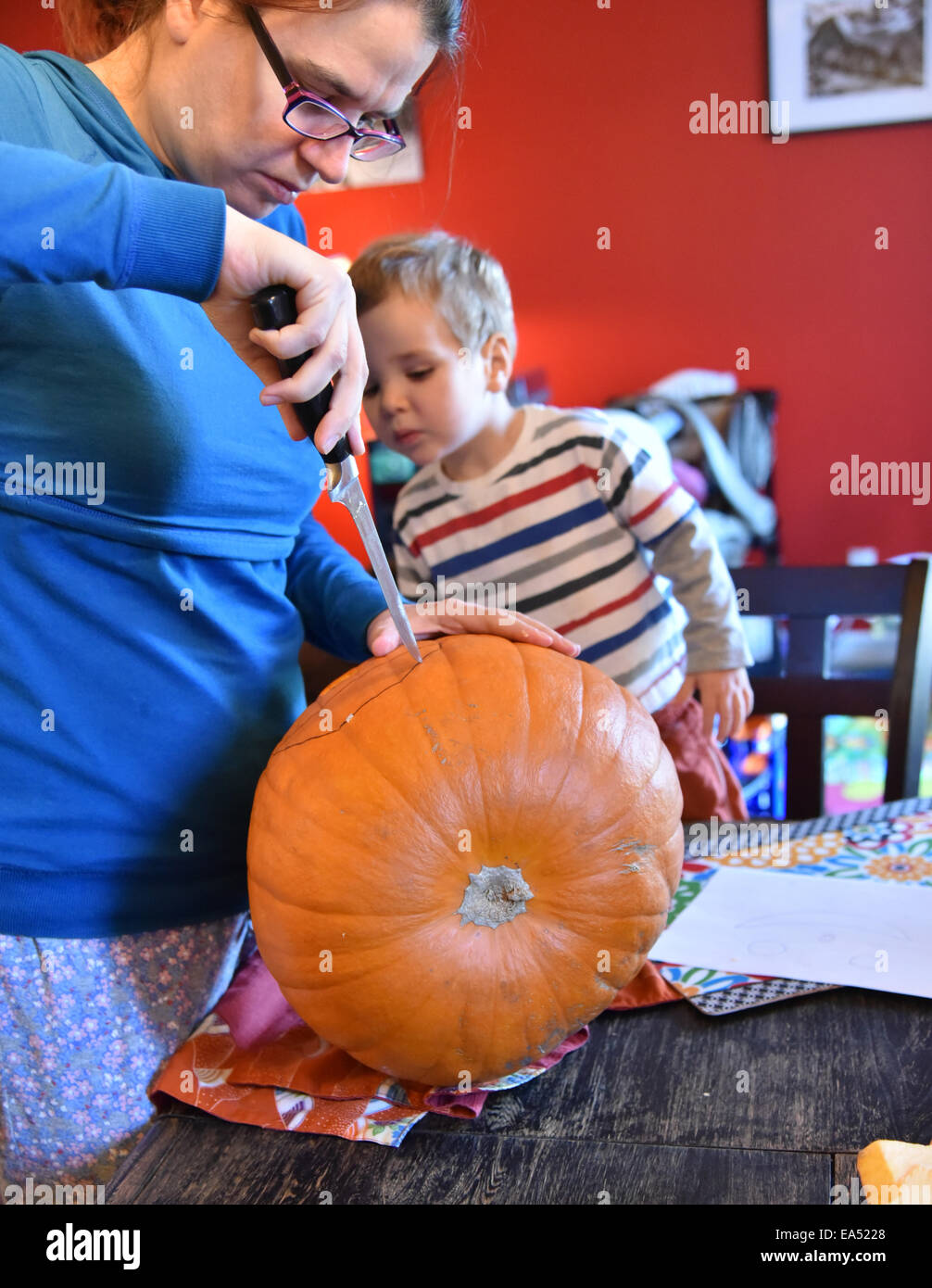 A mother carving a face in a pumpkin while her son watches Stock Photo
