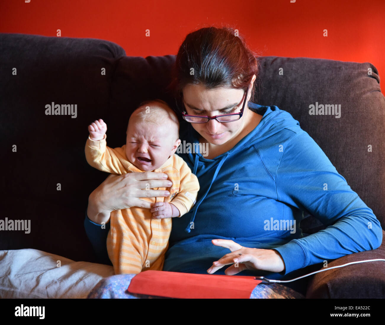A mother in pyjamas using an ipad and ignoring her crying baby Stock Photo
