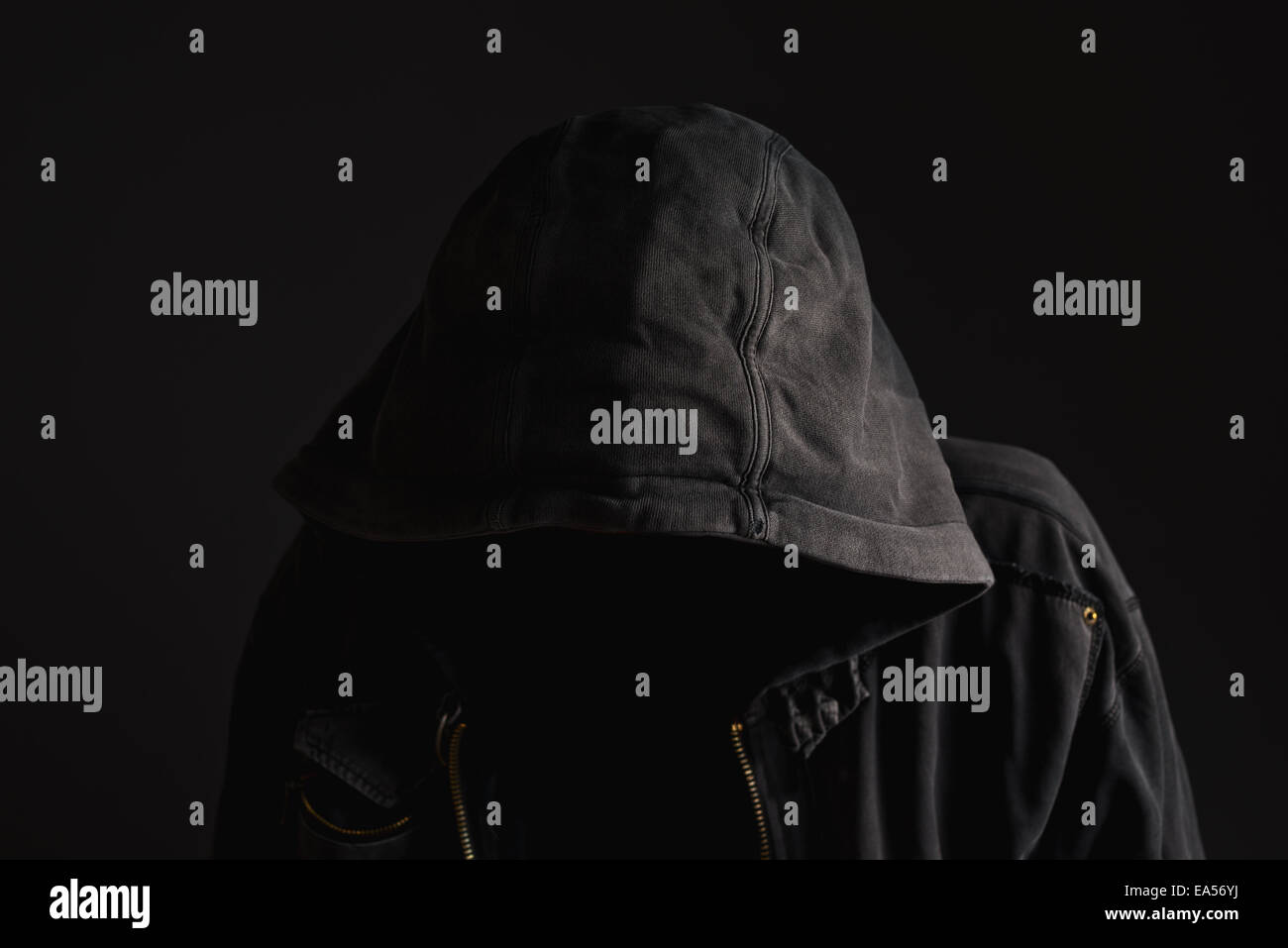 Faceless unknown and unrecognizable man without identity wearing hood in dark room, spooky criminal person. Stock Photo