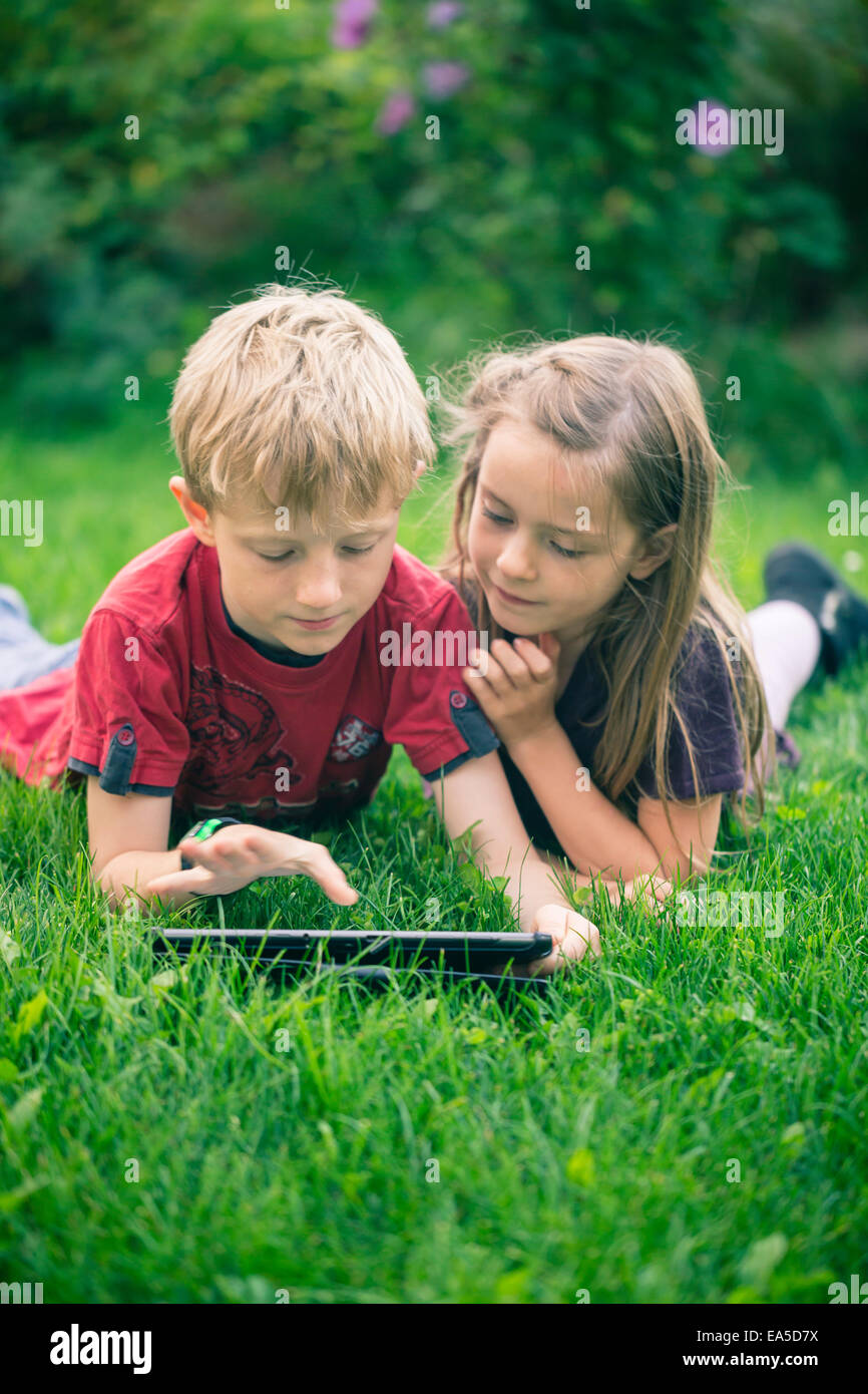 Brother and sister lying on a meadow using digital tablet Stock Photo ...