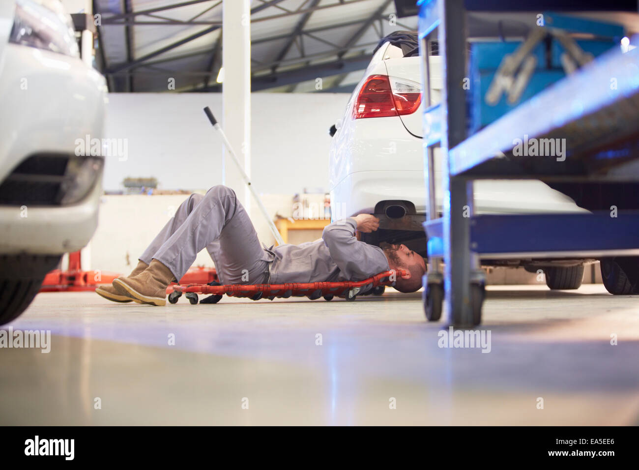 Car mechanic on creeper dolly at work in repair garage Stock Photo Alamy