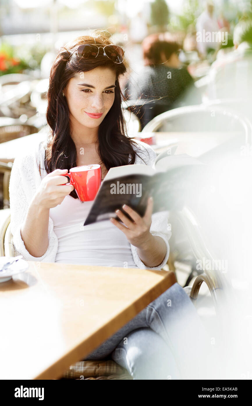 Smiling young woman reading a book at a pavement cafe Stock Photo - Alamy