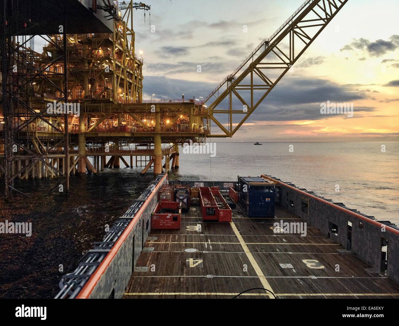 Nautical vessel approaching an oil platform at sunrise Stock Photo