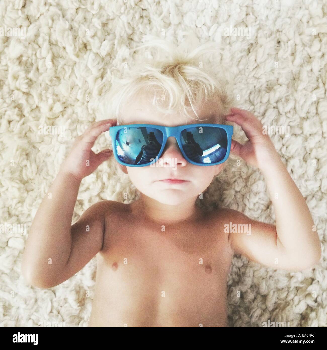 Boy lying on carpet wearing sunglasses Stock Photo