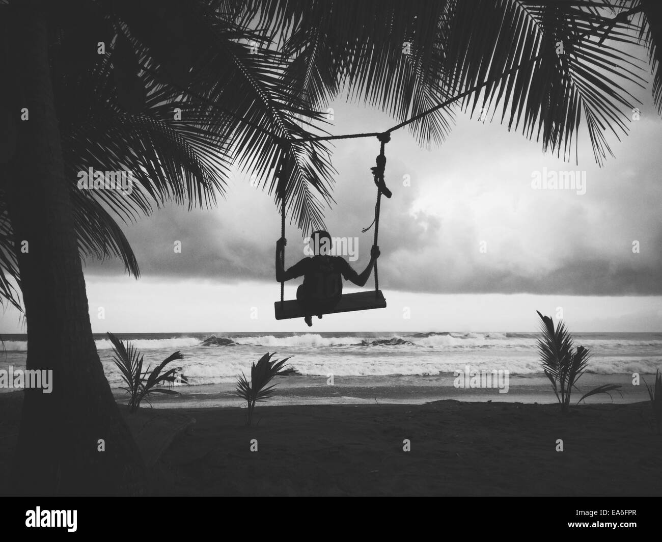 Silhouette of boy sitting on a swing on the beach Stock Photo