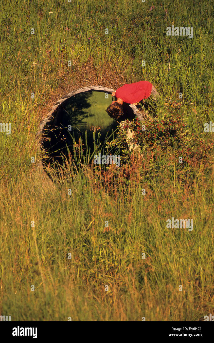 Curious young boy looking through a culvert in New Hampshire, USA. Stock Photo