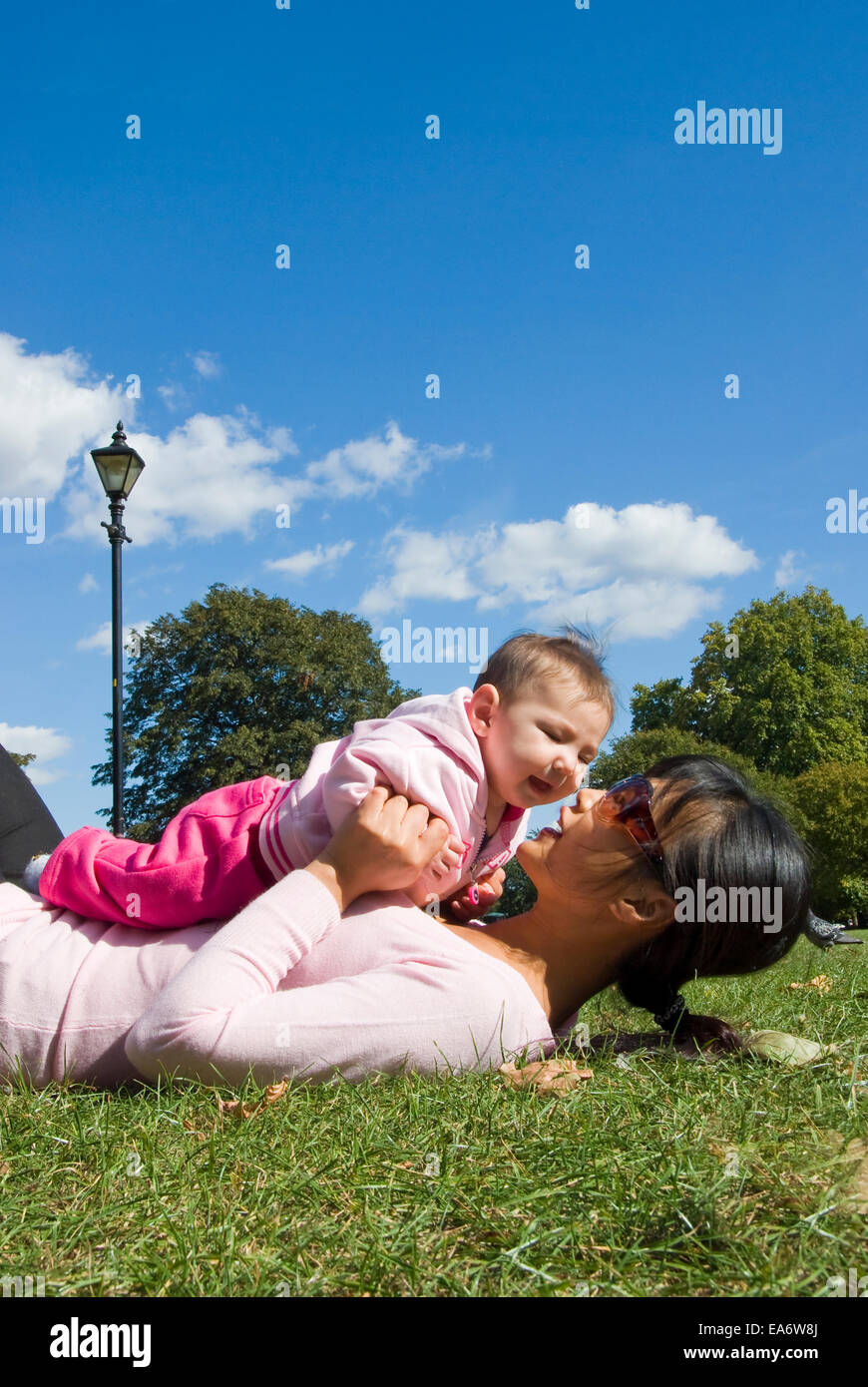 young Korean mother kissing mixed race (asian / caucasian) baby girl in park Stock Photo
