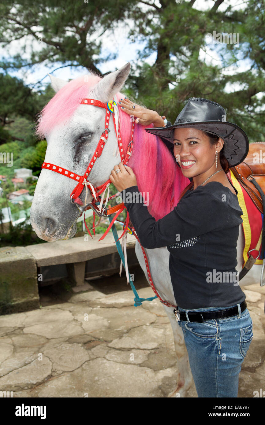 A beautiful Asian Filipina woman posing with a white horse with pink dyed mane at Mines View Park in Baguio City, Philippines. Stock Photo