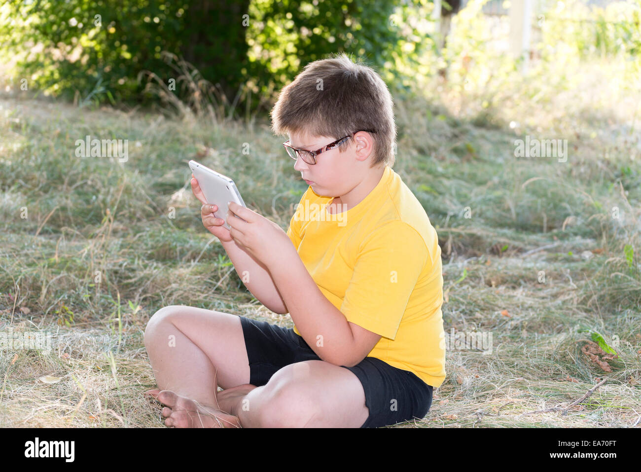 The boy in glasses looks tablet computer at nature Stock Photo