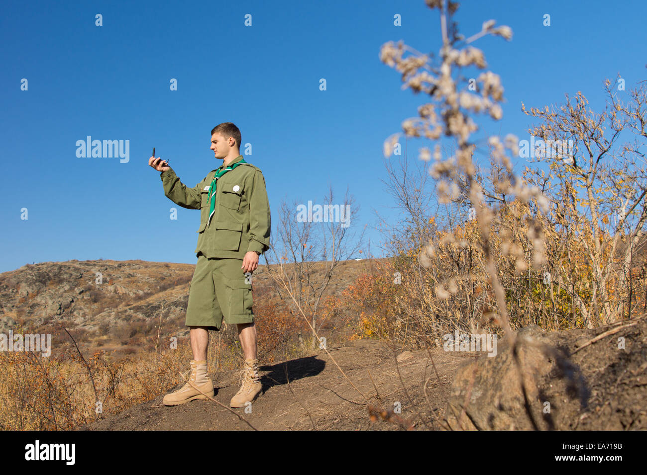 Scout standing on a rock taking a compass reading to establish his location and determine the direction of his route Stock Photo