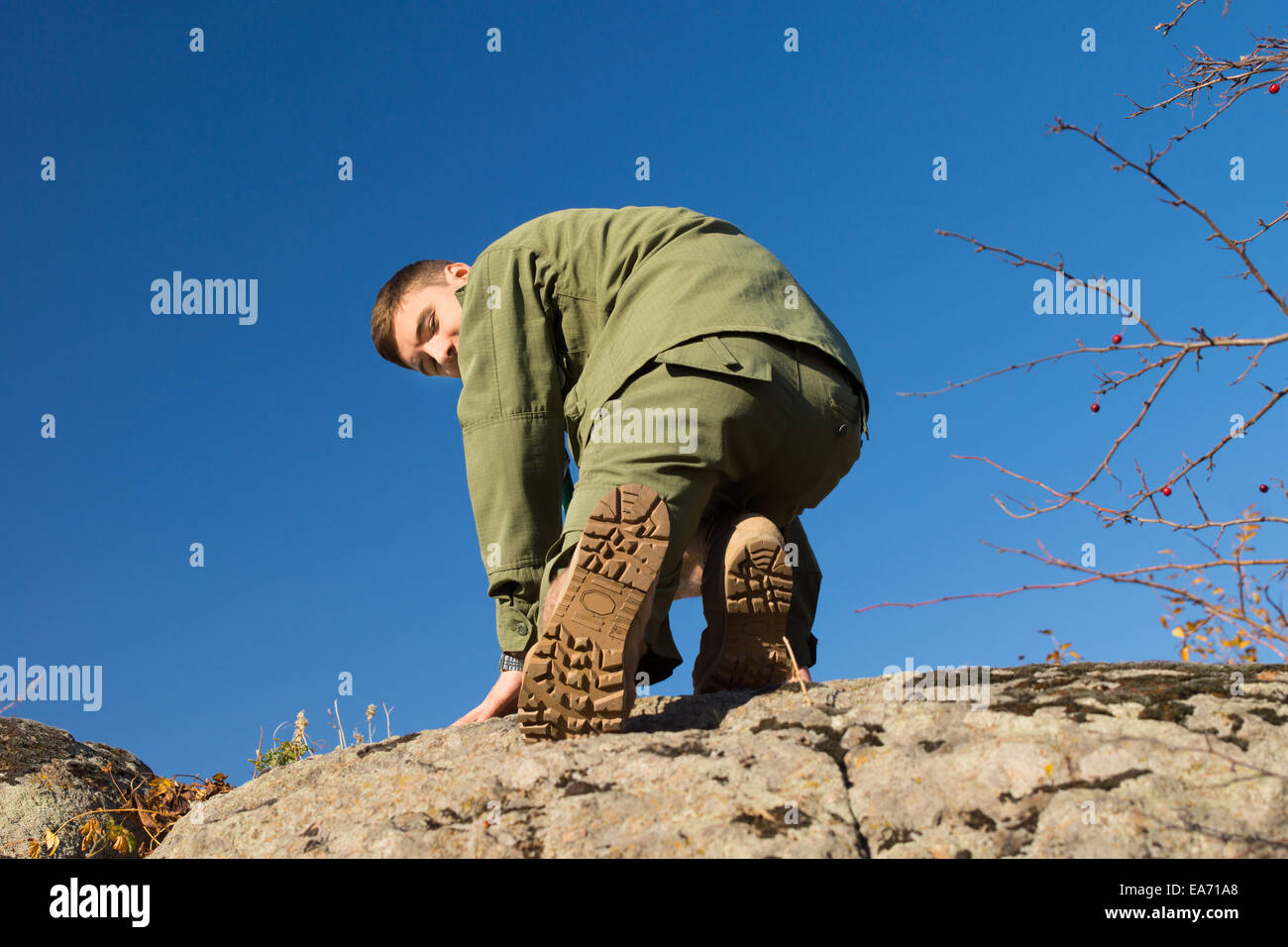 Young Handsome Boys Scout Climbing on a Big Rock While Looking at the Camera. Captured on a Blue Sky Background. Stock Photo