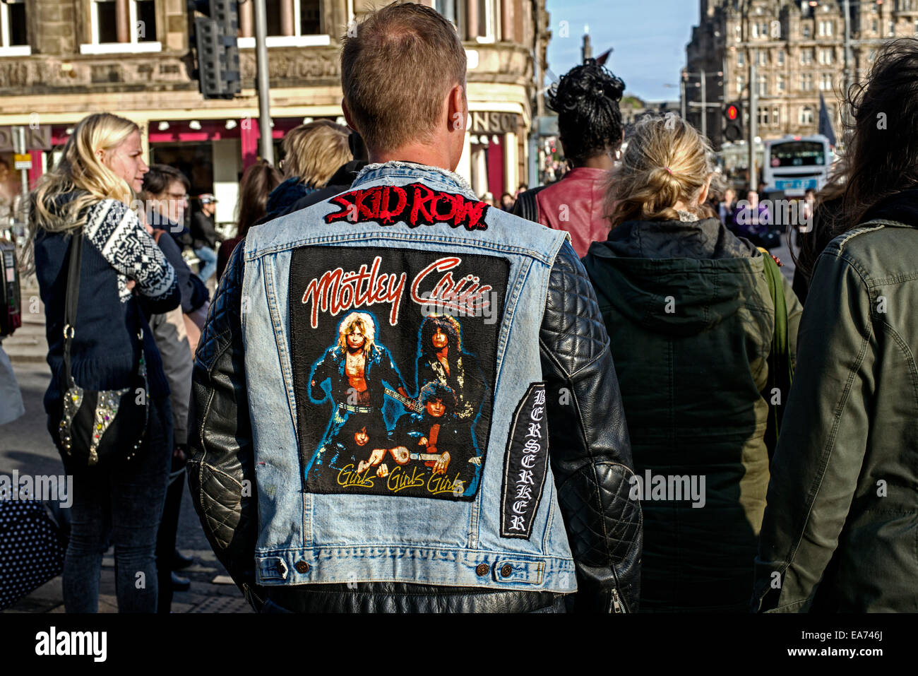 The back view of a young man wearing a black leather and denim jacket featuring the heavy metal bands Motley Crue and Skid Row. Stock Photo