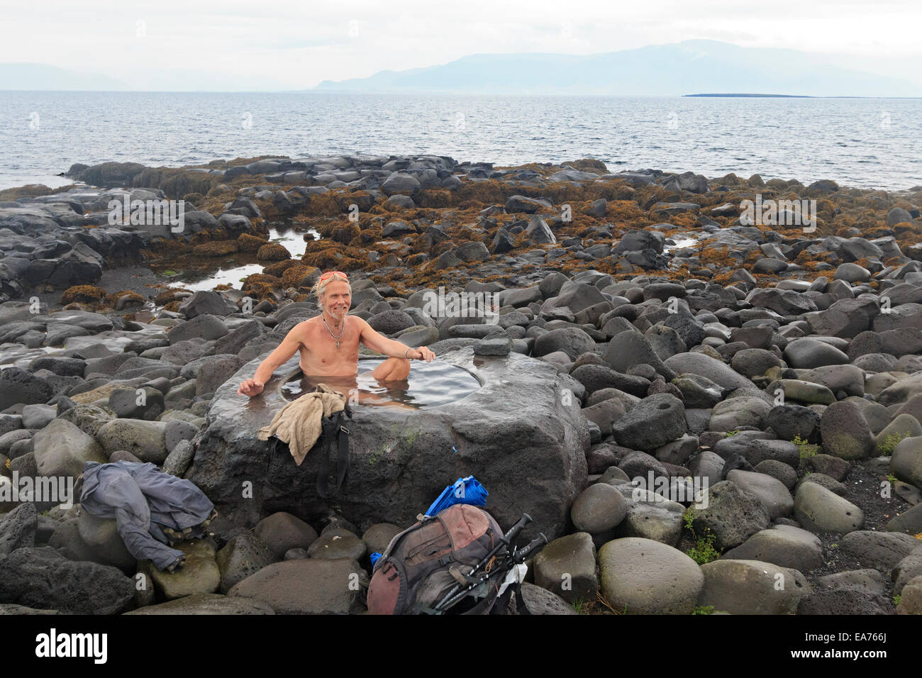 Local man bathes in a natural hot spring set in rocks at the shoreline of Reykjavik's waterfront. Stock Photo