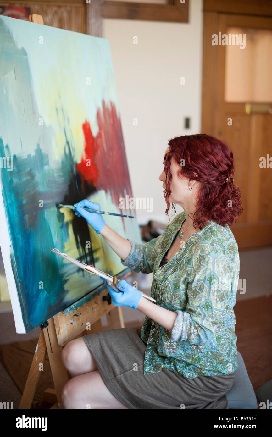Middle-aged woman holding palette and painting on canvas Stock Photo