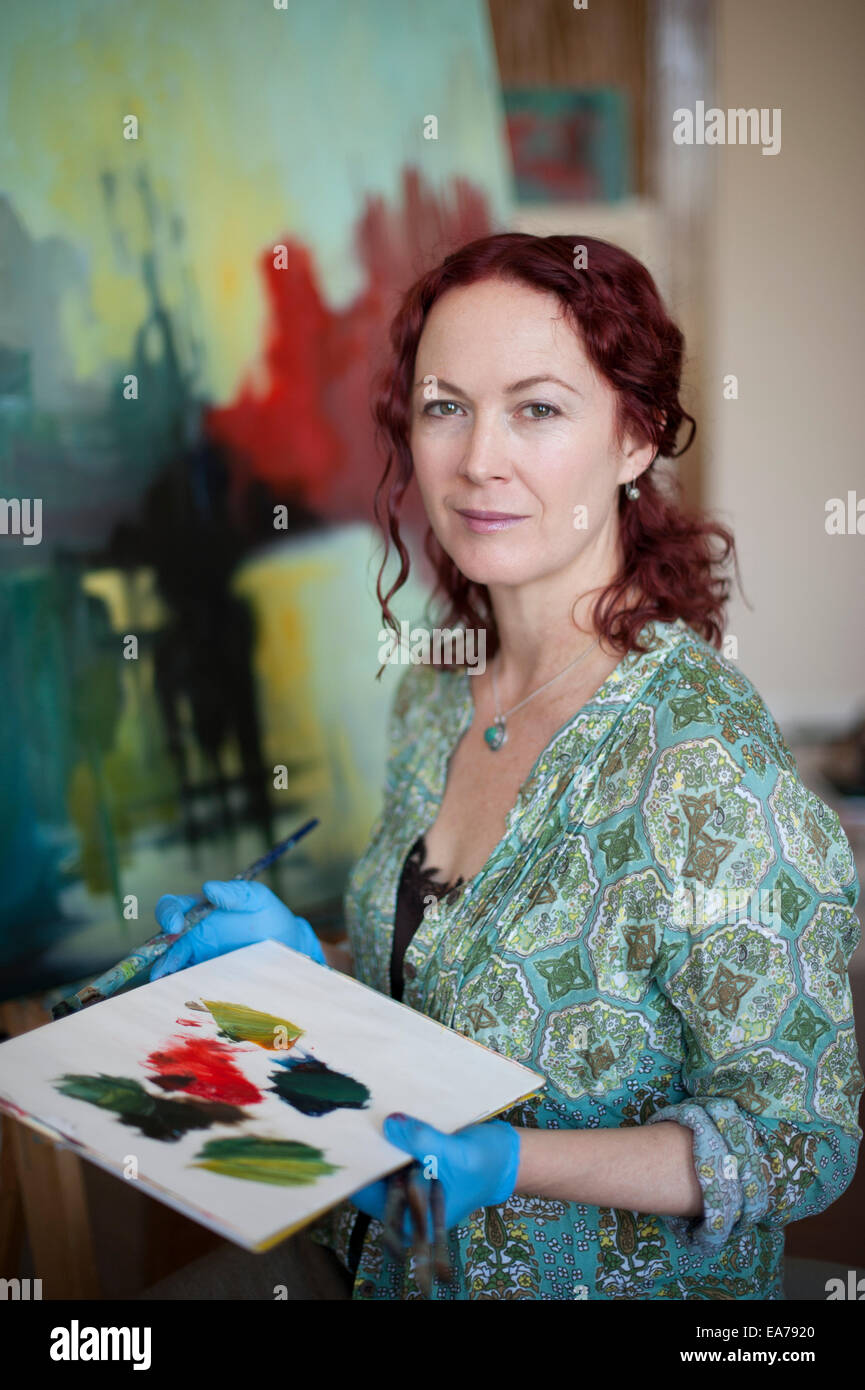 Portrait of middle-aged woman holding palette standing in front of canvas Stock Photo