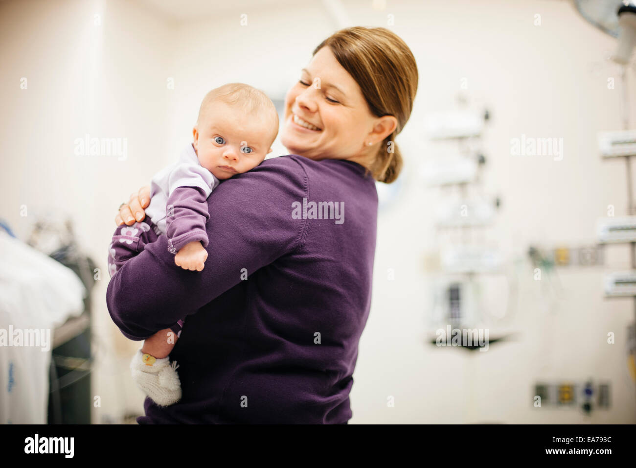 Mother standing in hospital ward holding baby son (6-11 months) Stock Photo