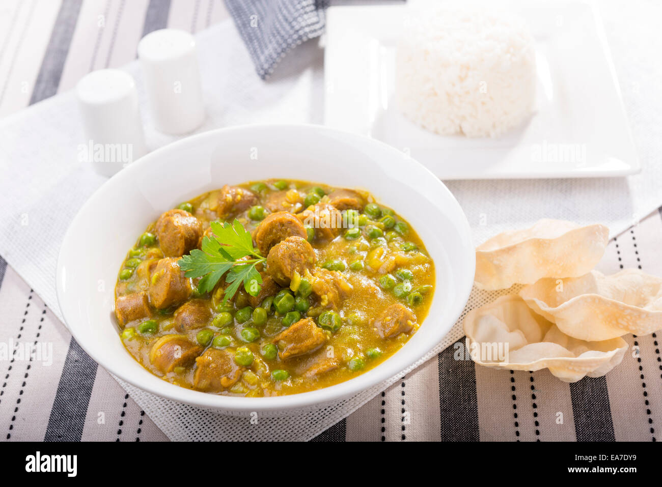 Large bowl of curried sausages with peas and a side of rice and papadum Stock Photo