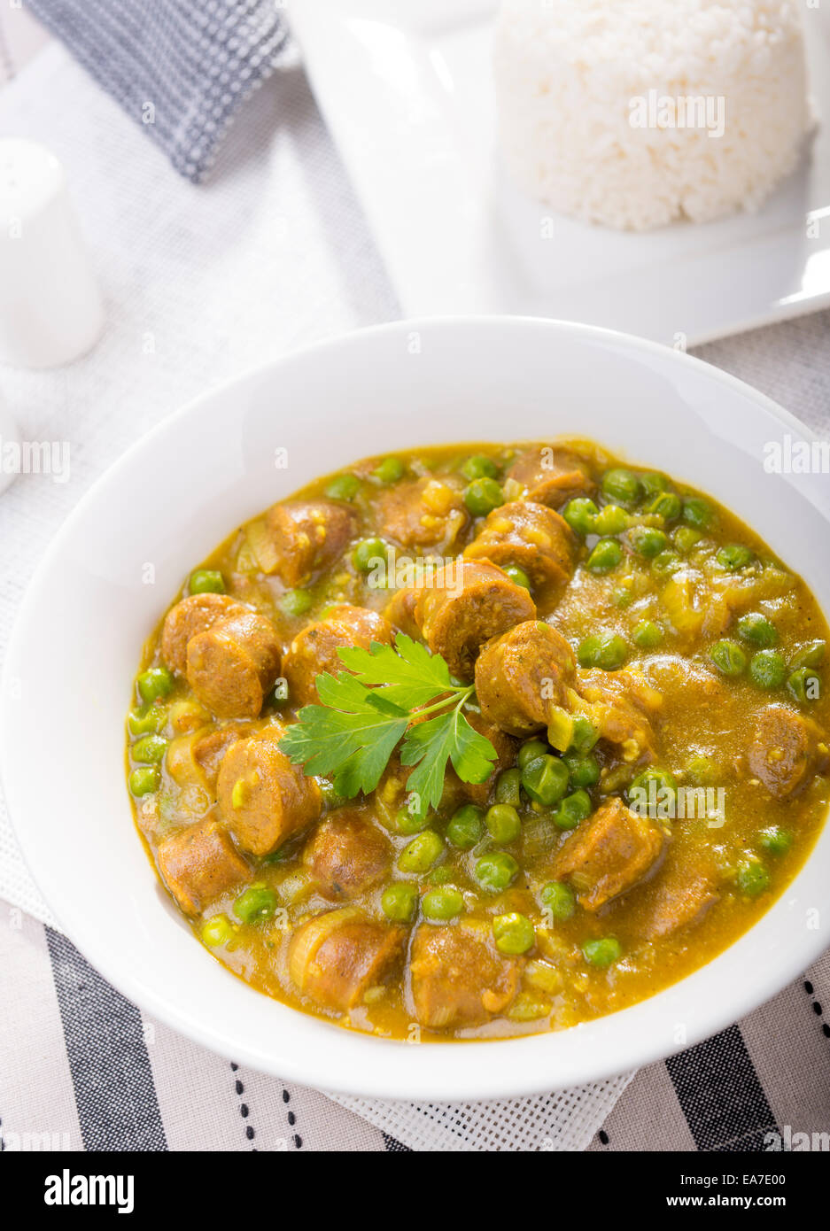 Large bowl of curried sausages with peas and a side of rice Stock Photo