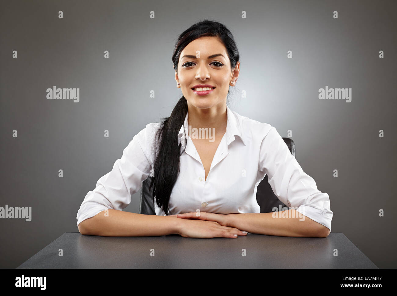 Hispanic business woman sitting at her desk smiling Stock Photo - Alamy