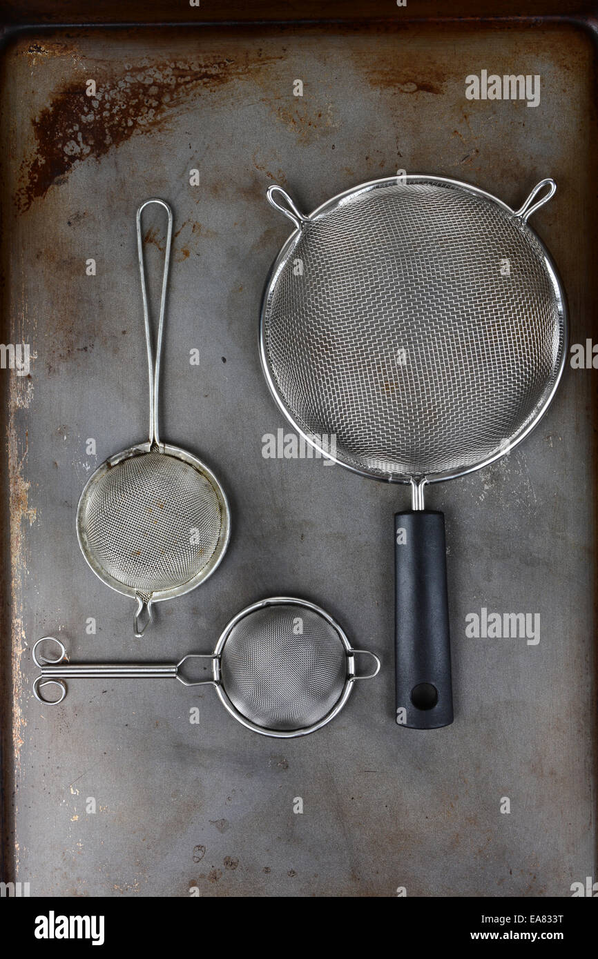 Kitchen strainers on an old used cookie baking sheet. Vertical format shot from a high angle. Stock Photo