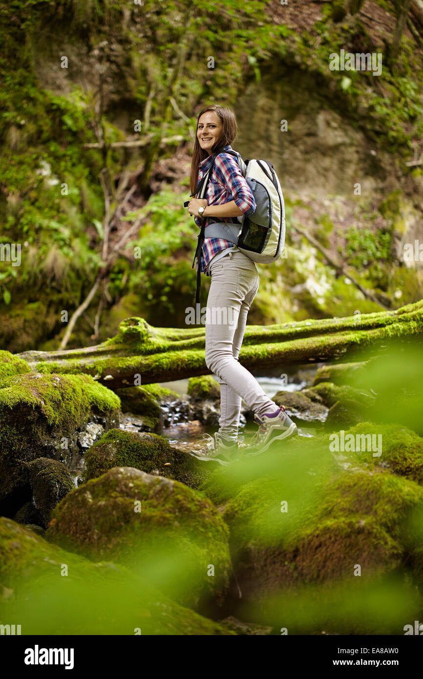Young woman hiker with backpack crossing a river among boulders covered ...