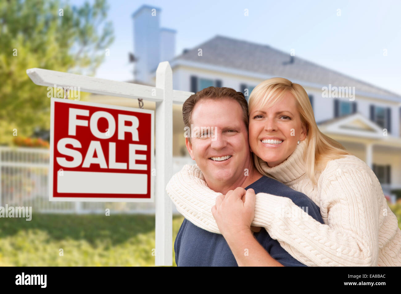 Affectionate Happy Couple in Front of New House and For Sale Real Estate Sign. Stock Photo