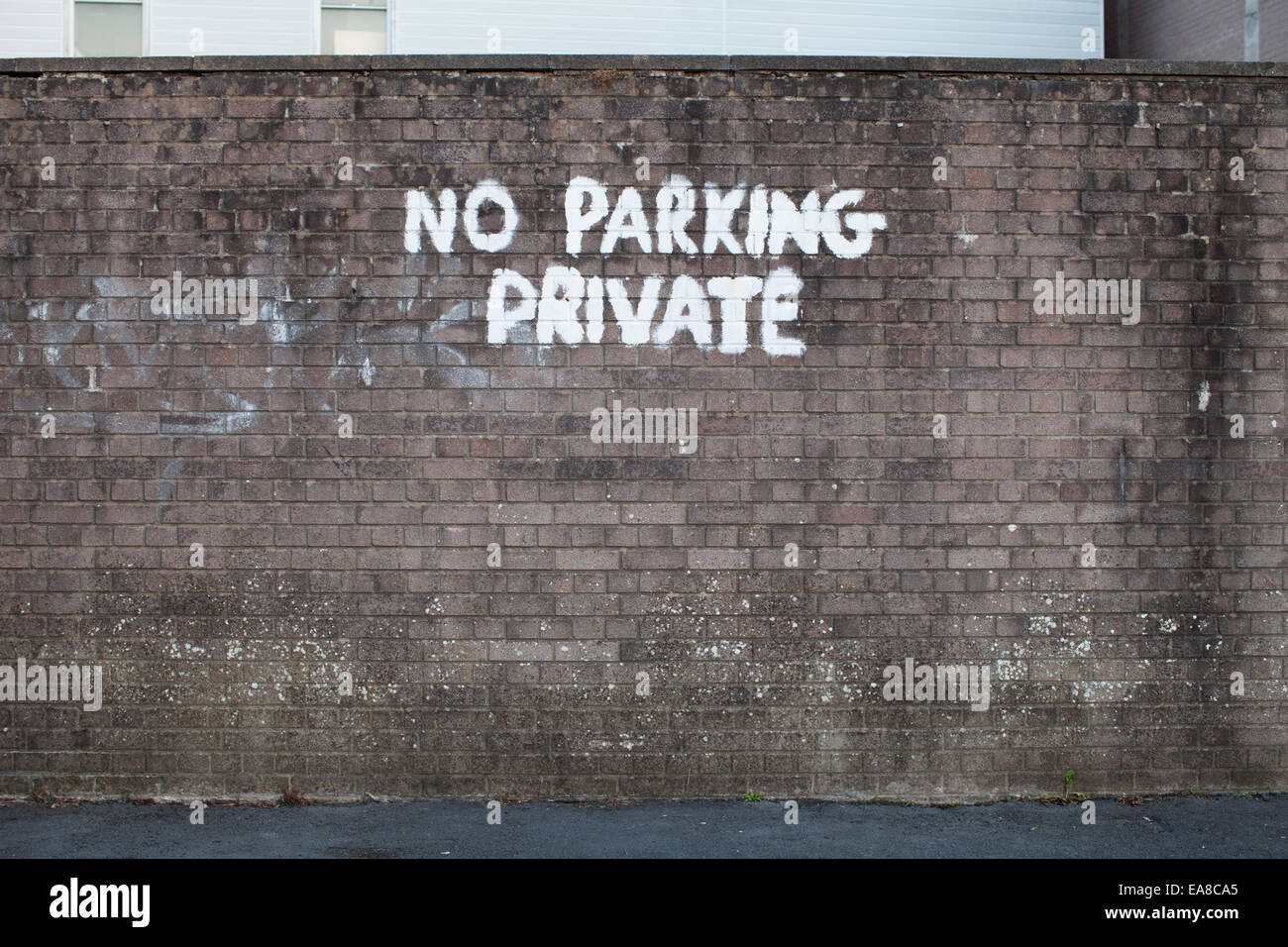 No parking private spray painted graffiti onto a grungy brick wall in white paint. Stock Photo