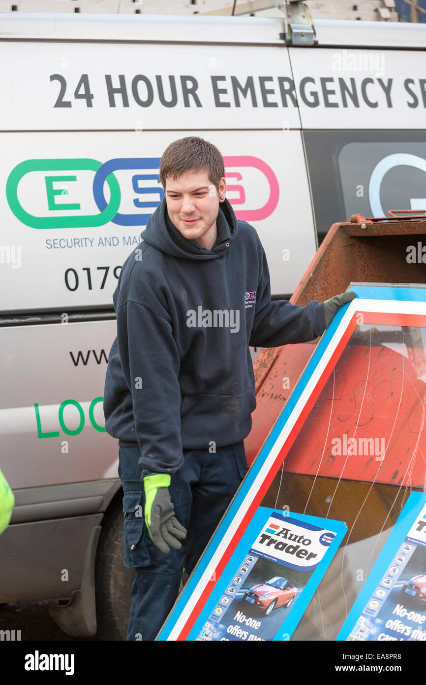 Workmen repairing broken shop window glass and disposing of the broken