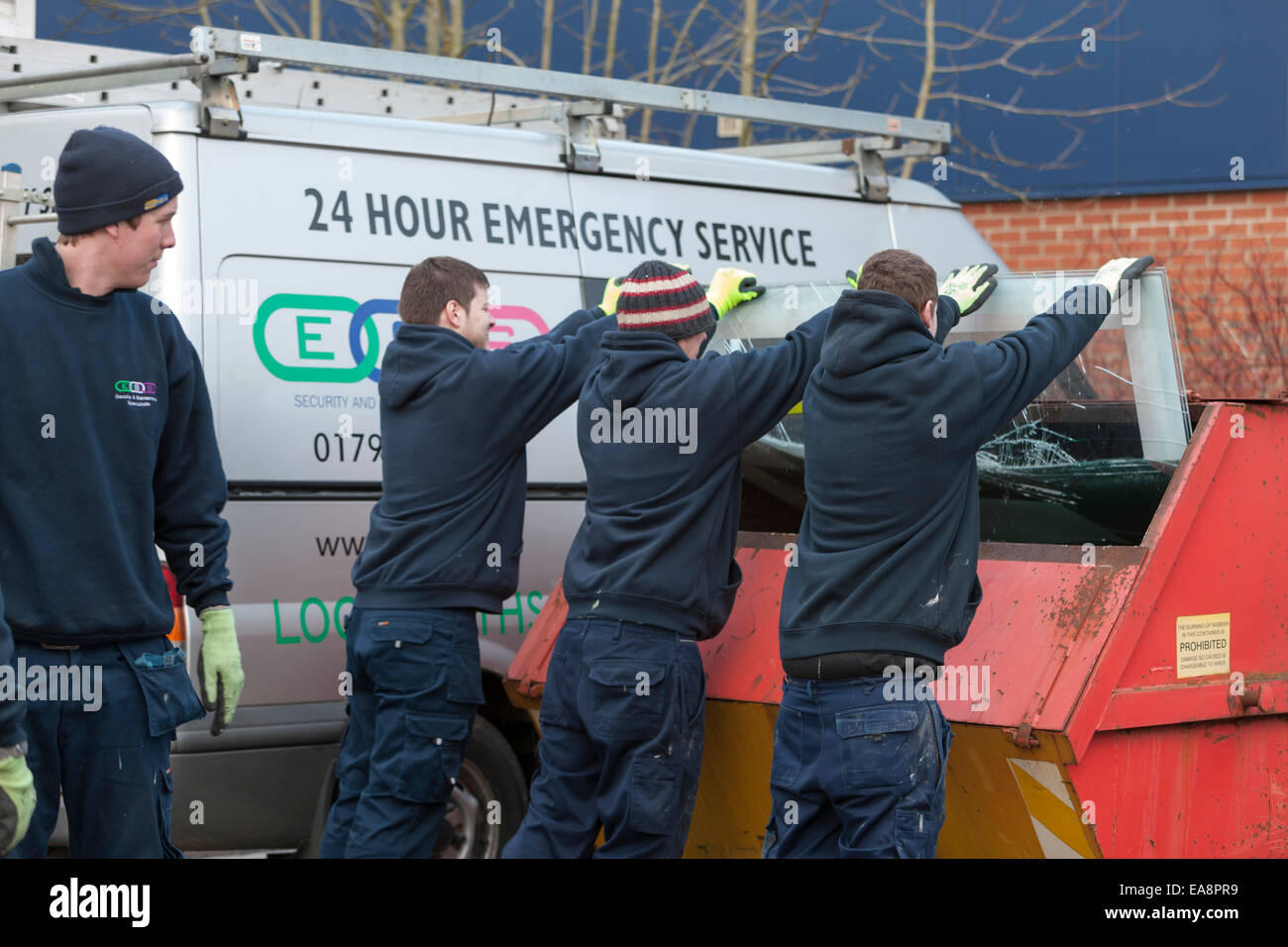 Workmen repairing broken shop window glass and disposing of the broken
