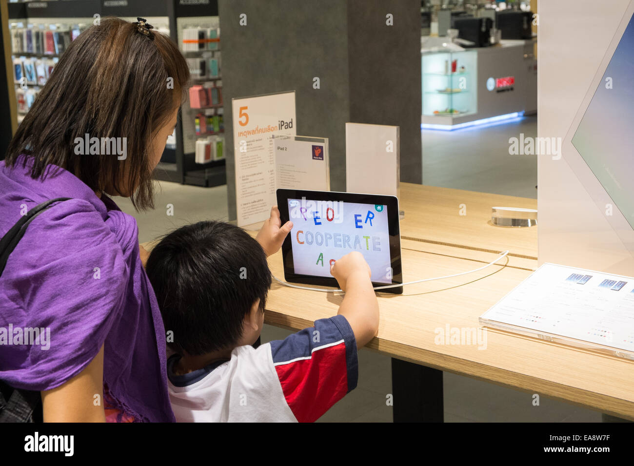 Girl using,testing,checking out an Apple ipad computer with her mother at electronics department at Central World Plaza,Bangkok Stock Photo