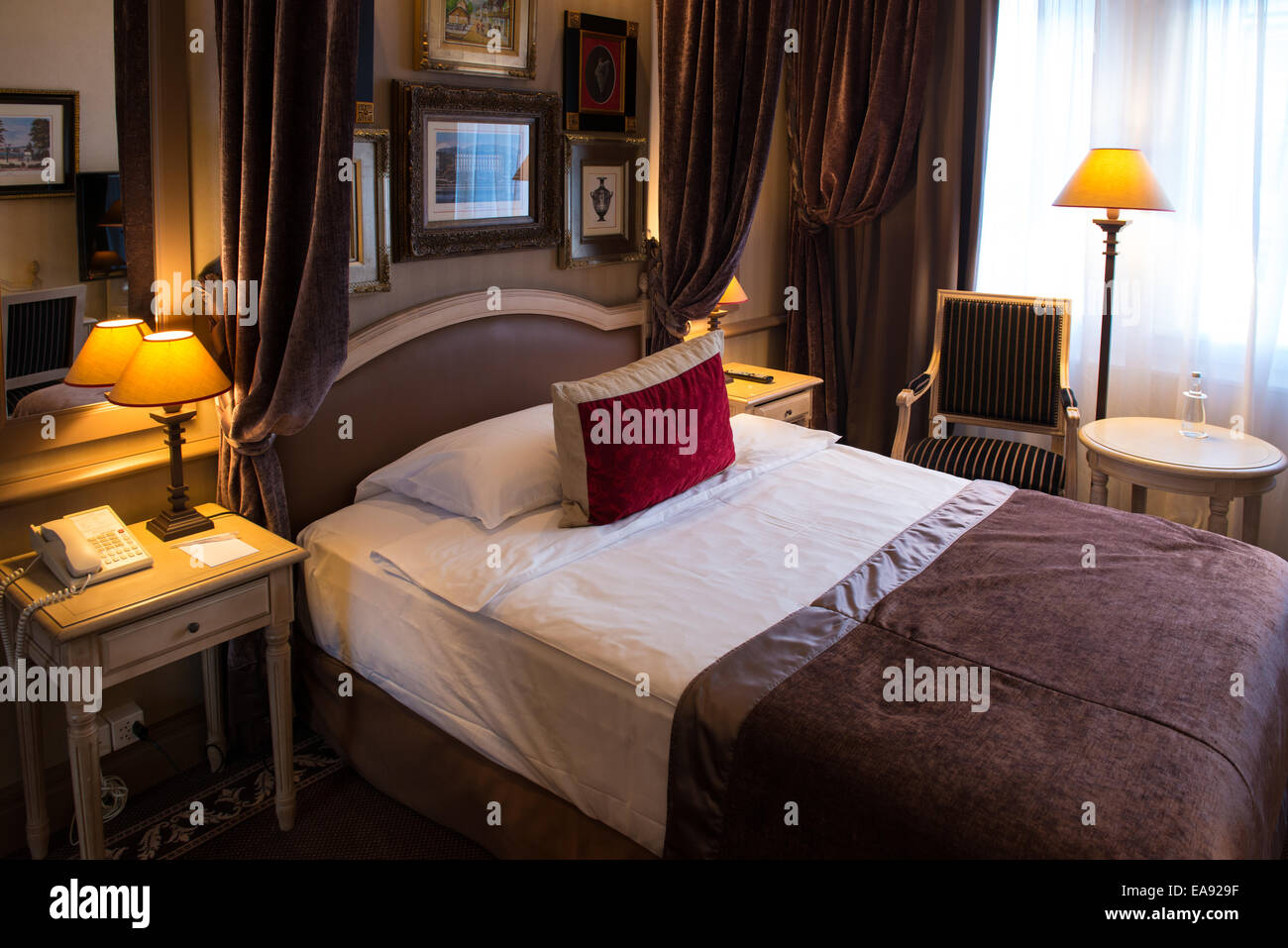 luxurious hotel room with a bed covered with a brown jacket and red pillow Stock Photo