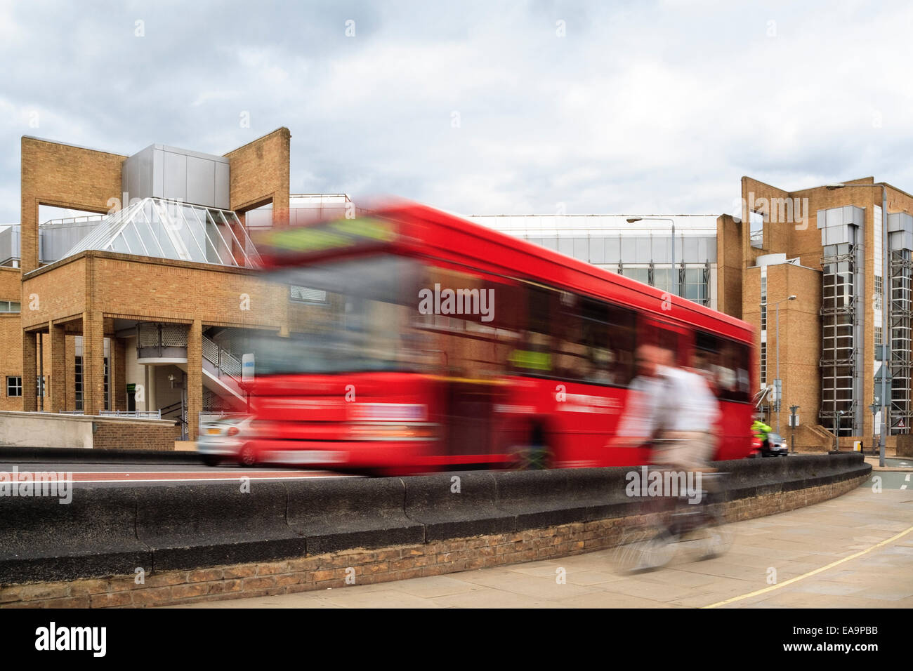 blurred motion image of cyclist and red bus in Kingston, London, UK - Cycle lane separated from traffic by a wall. Stock Photo