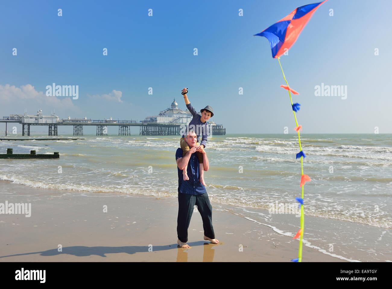 Grandfather with grandson flying a kite on the beach at Eastbourne. East Sussex. UK Stock Photo