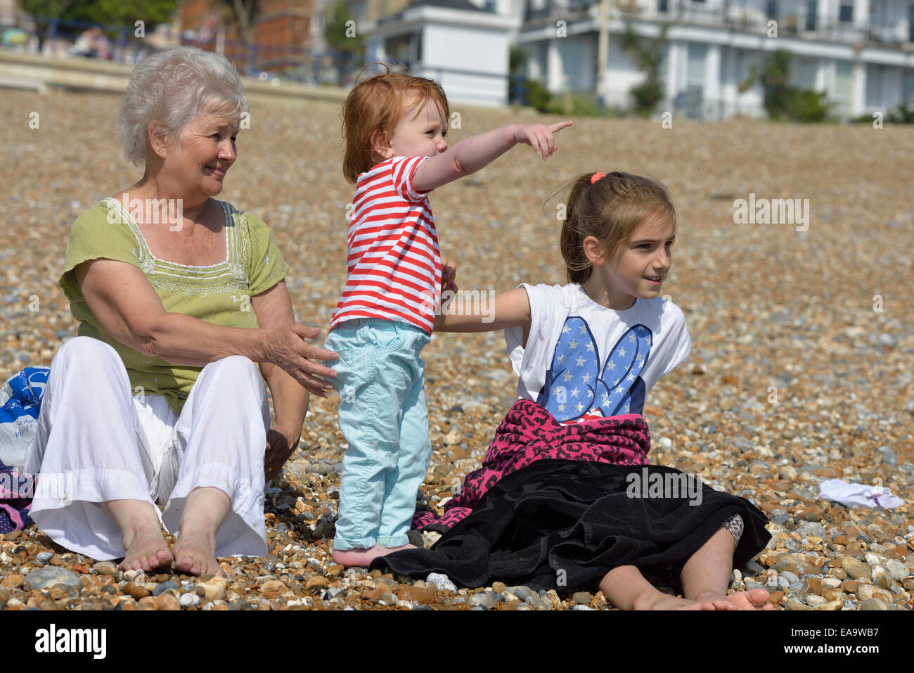 Grandmother with two grandchildren sitting on Eastbouren beach. East Sussex. UK Stock Photo