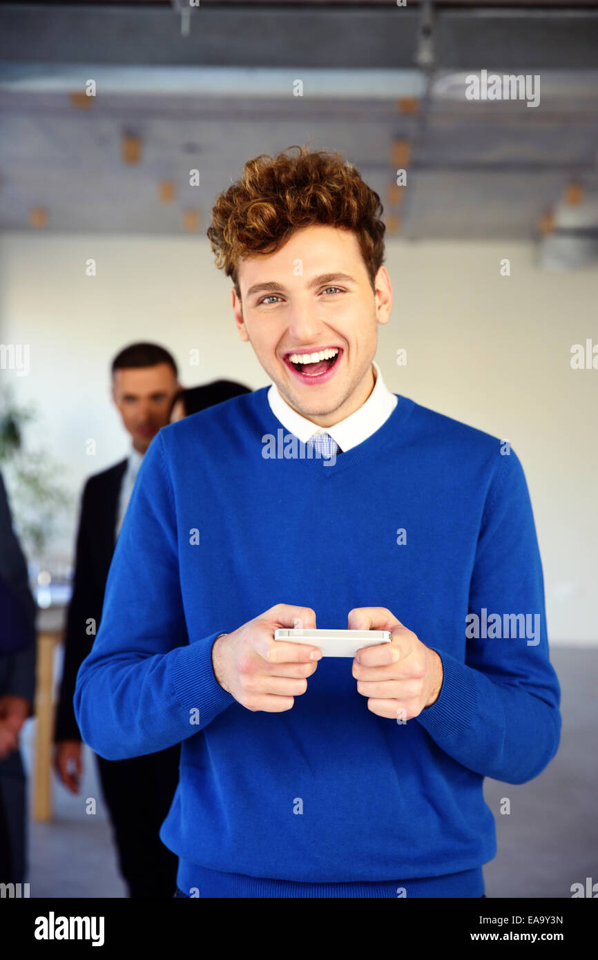 Laughing young businessman standing with smartphone in office Stock ...