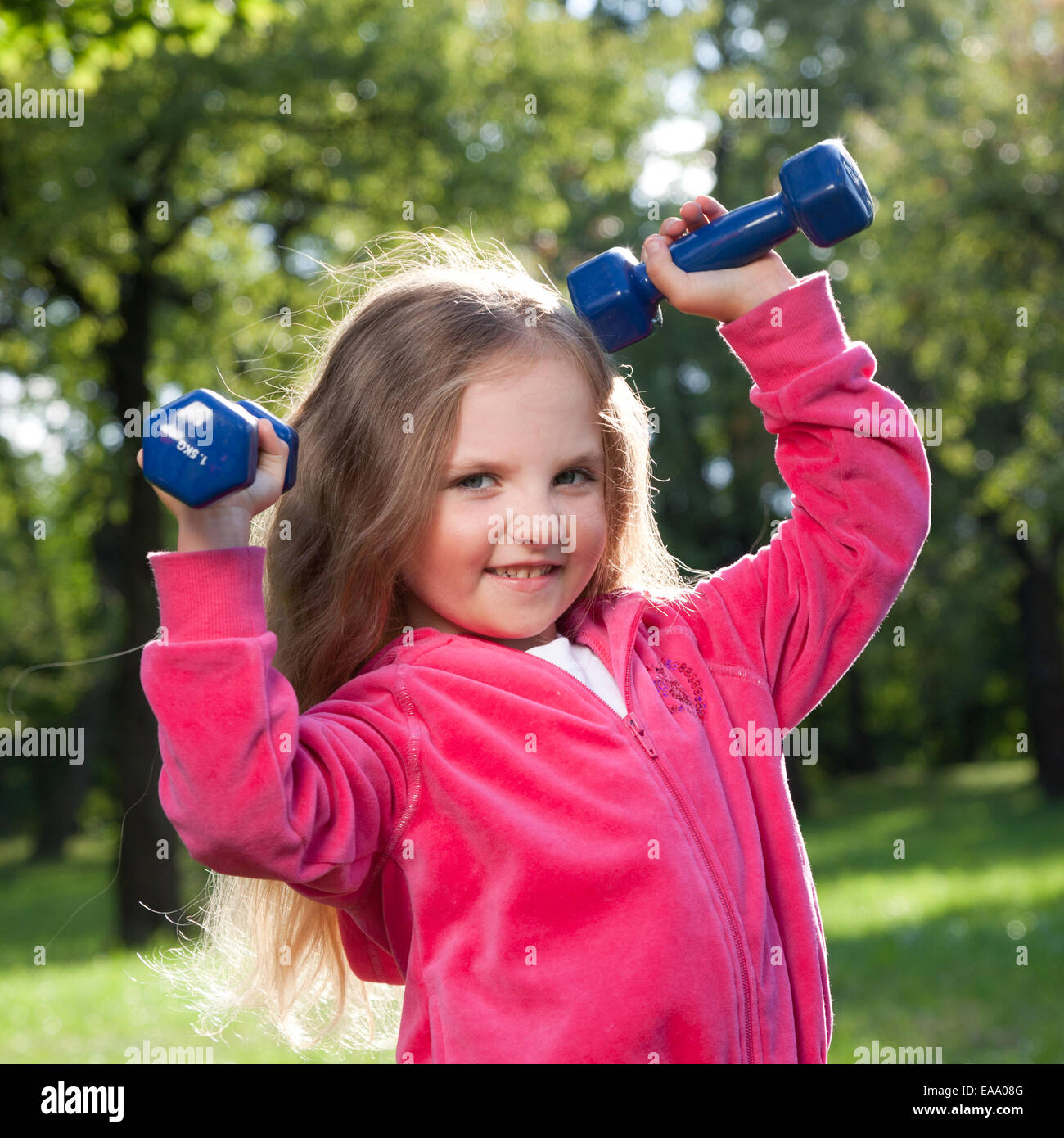 Happy little girl lifting dumbbells in park outdoors Stock Photo