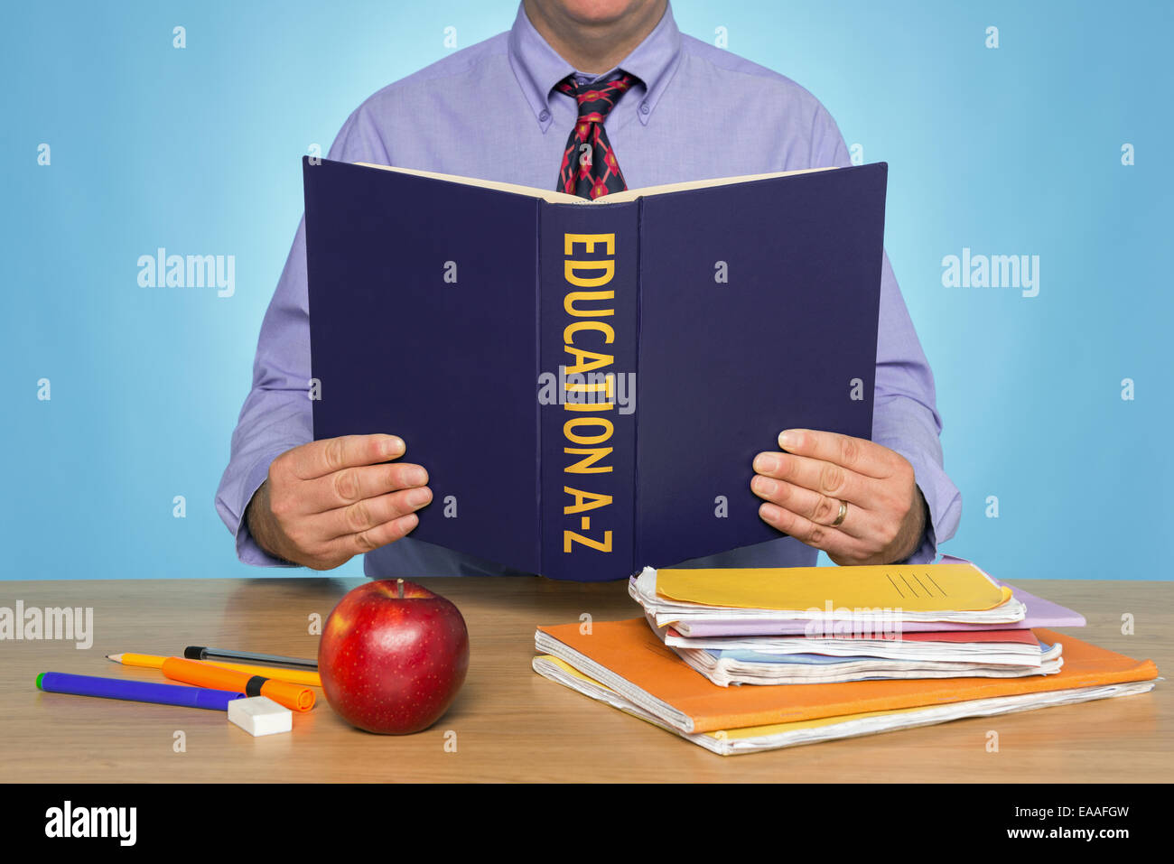 A teacher sat at a desk reading an EDUCATION A-Z book. Stock Photo