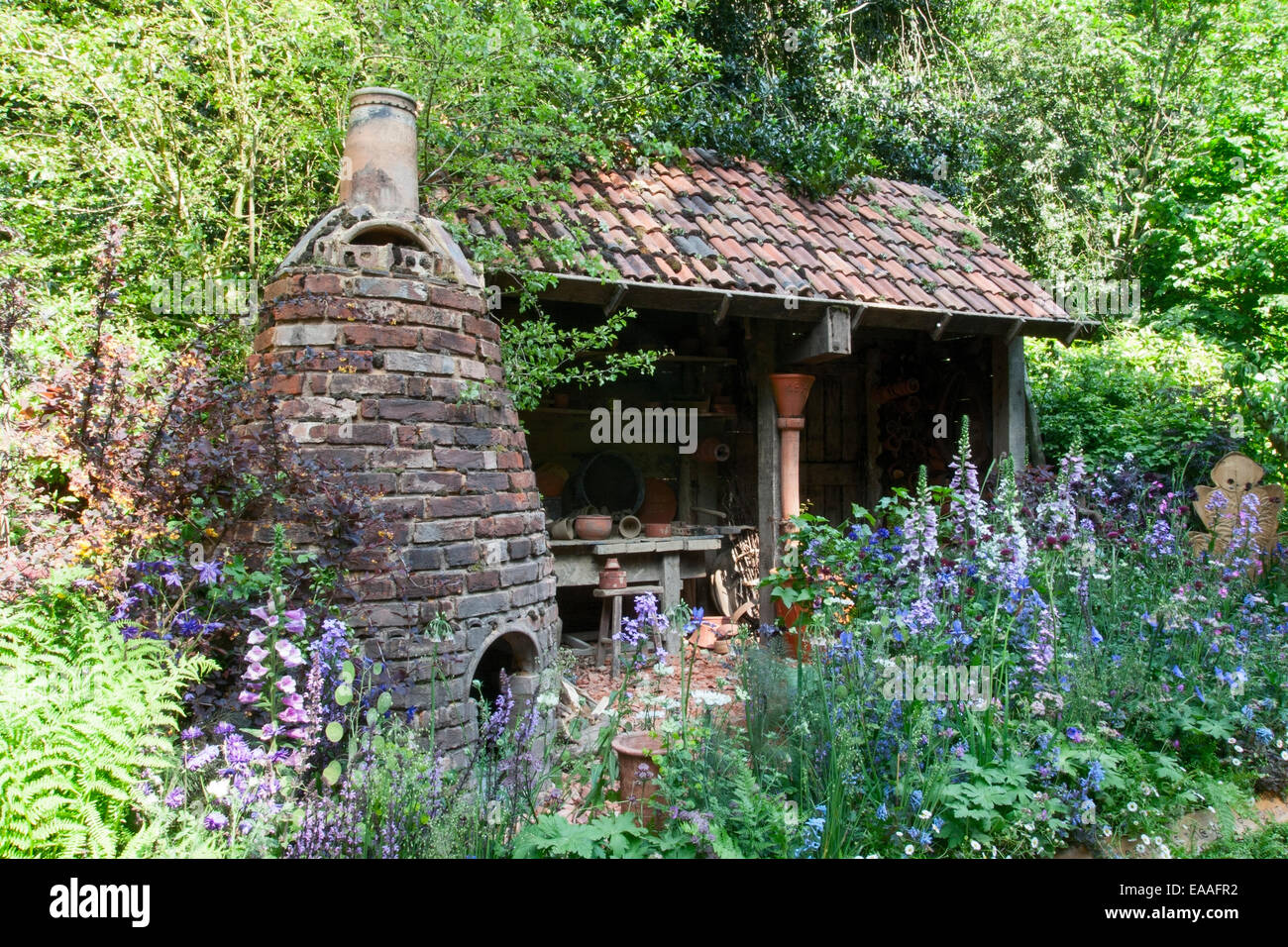 Chelsea Flower Show 2014. An old potting shed with perennial and bulb planting. Brick kiln on the left. Stock Photo