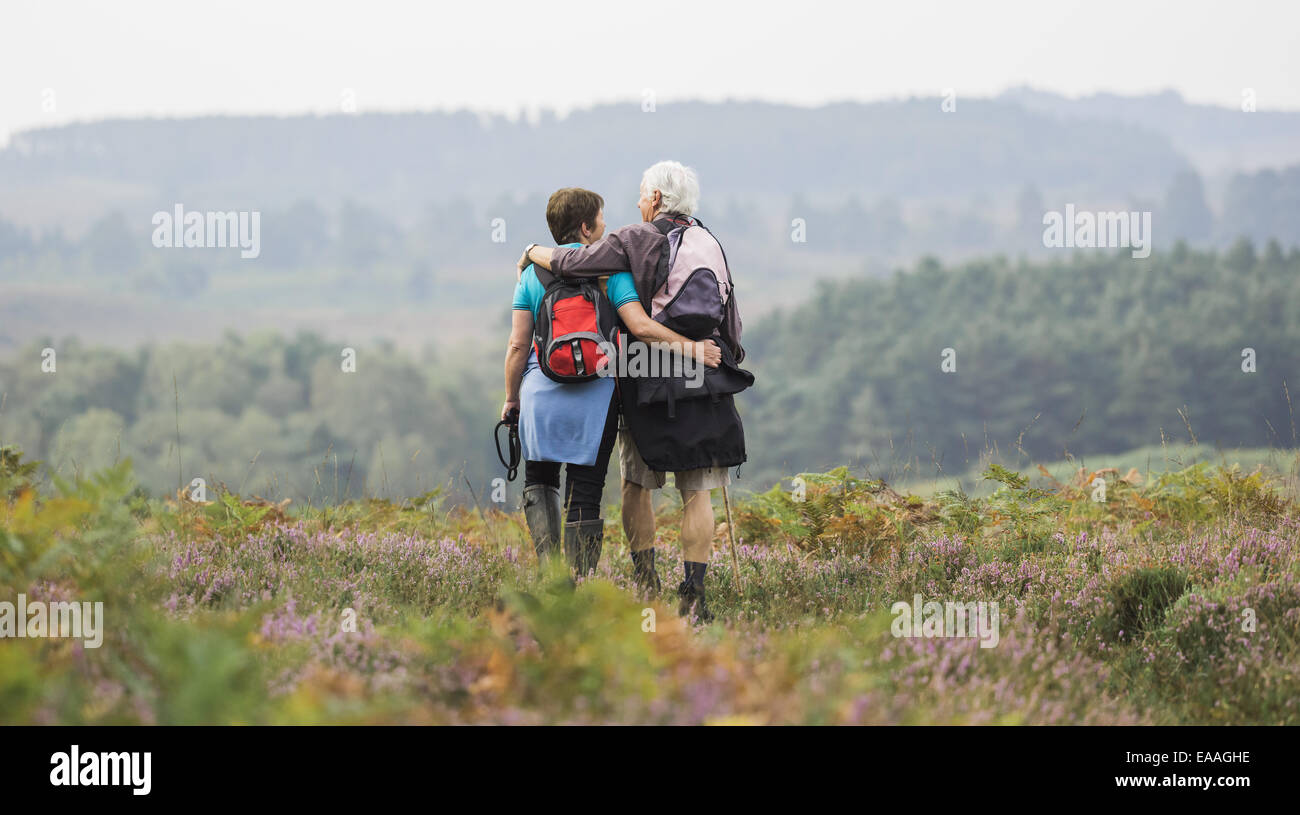 A couple standing on a path looking at the view over wooded hills, with arms around each other. Stock Photo
