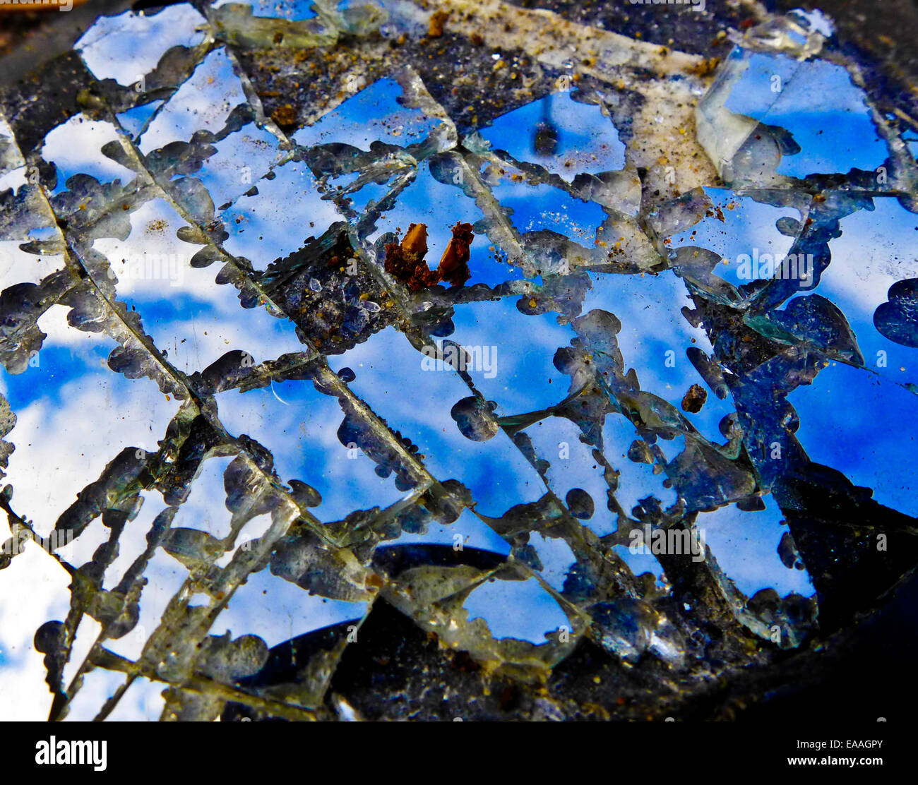 A car wing mirror lies shattered in the road reflecting the blue sky and clouds above. Stock Photo
