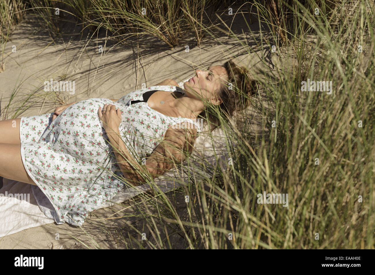 A pregnant woman lying in the sun in the sand dunes. Taking it easy